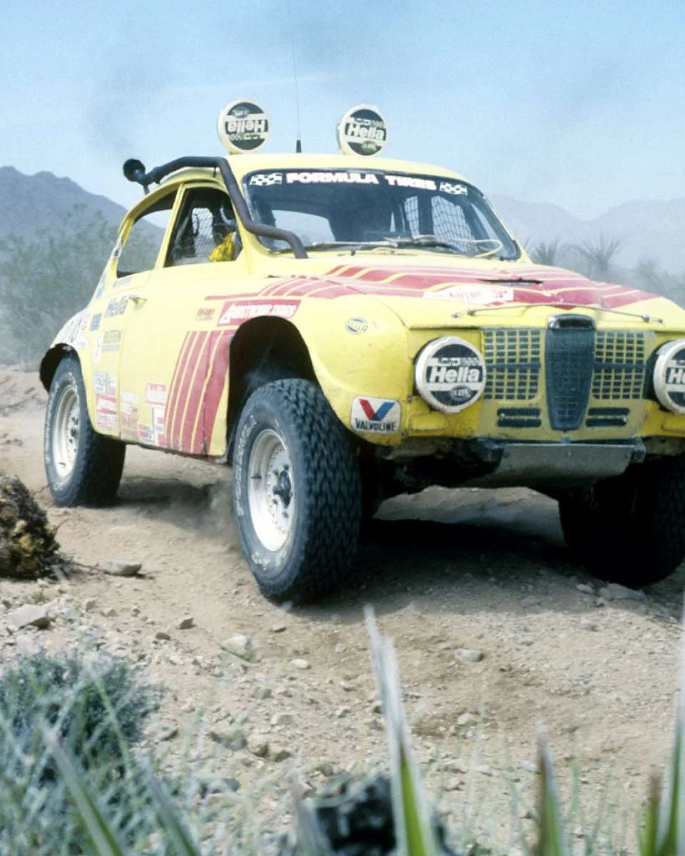 A rally car on dirt with roof-mounted lamps